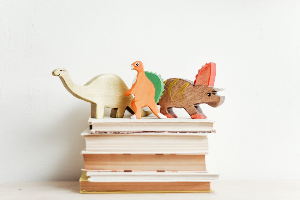 Drei Holz-Dinosaurier auf einem Stapel Bücher.