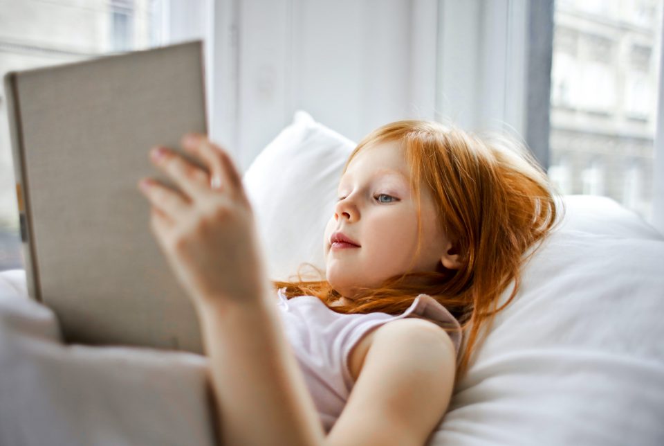 Mädchen mit Buch im Bett.