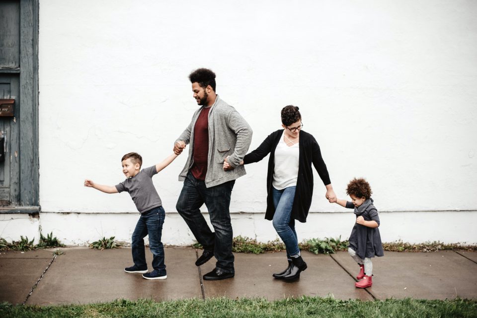 Mann mit Frau und Kindern halten sich an den Händen und spazieren in einer Reihe.
