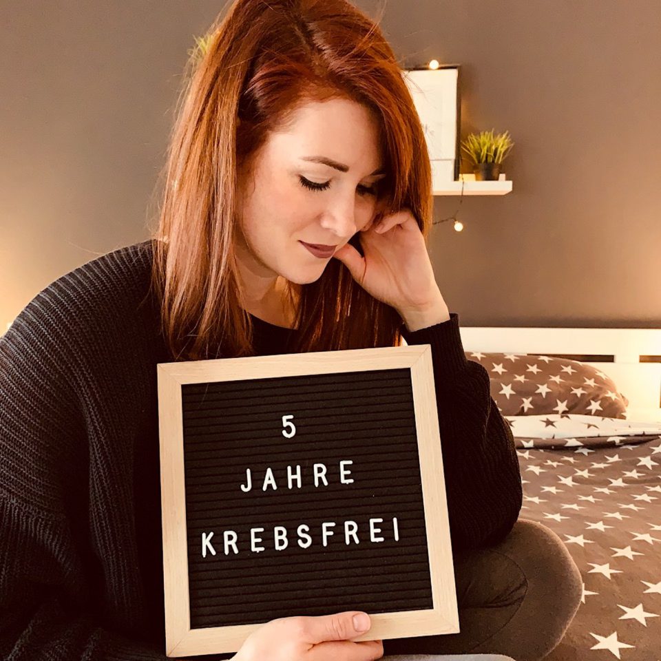 Frau mit Schild „5 Jahre krebsfrei“. Frau mit Schild „5 Jahre krebsfrei“.