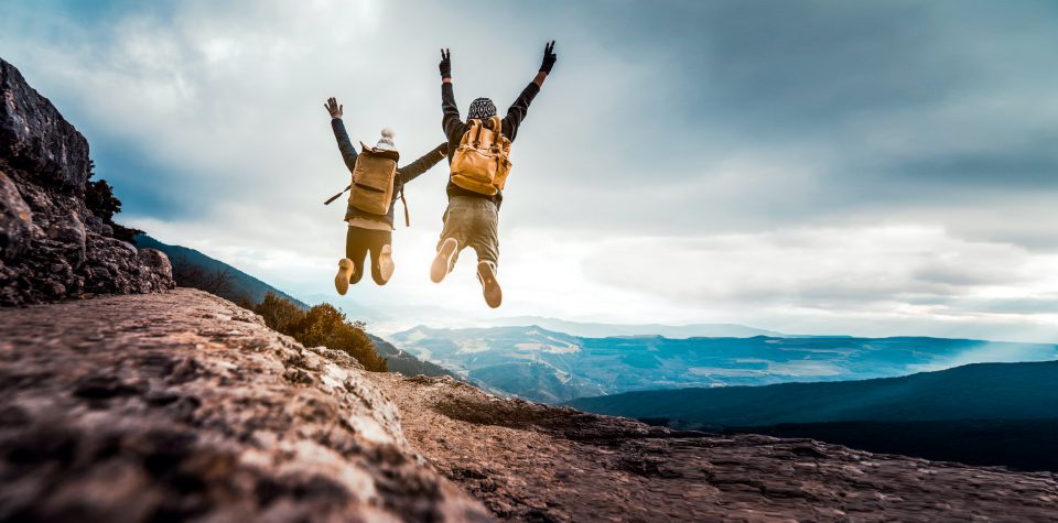 Zwei Menschen mit Rucksäcken springen beim Wandern in die Luft.