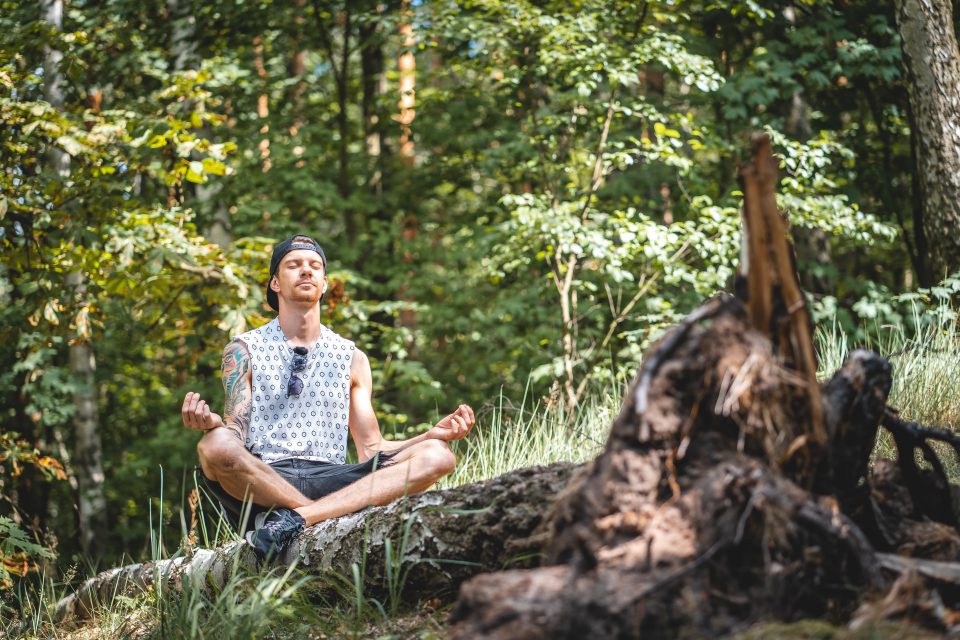 Mann sitzt auf Baumstamm im Wald und meditiert