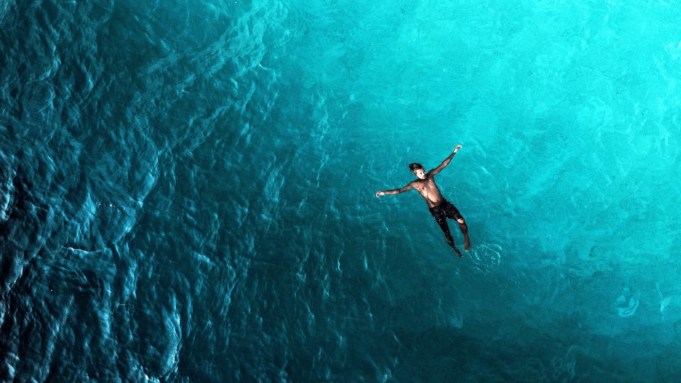 Ein Mann treibt mit ausgestreckten Armen rücklings im offenen Meer und zieht das Bein zu einer Schwimmbewegung an.