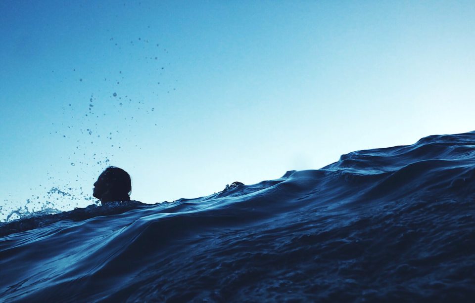 Eine Frau schwimmt nach Sonnenuntergang im Meer, es ist nur ihr Kopf zu sehen, das Wasser ist tiefblau.