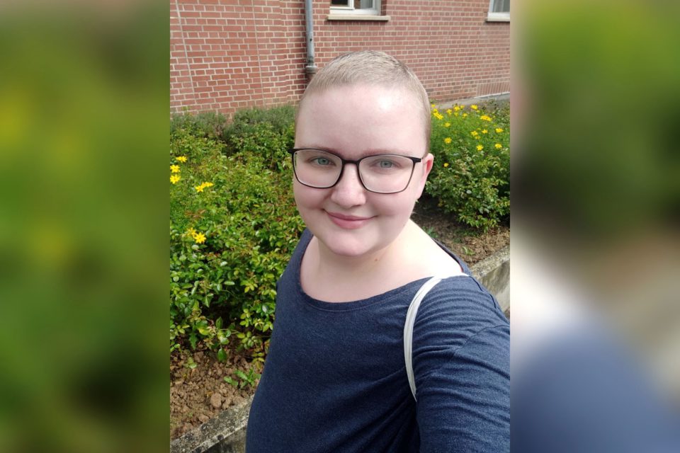 Frau mit Kurzhaarfrisur vor einem Blumenbeet.