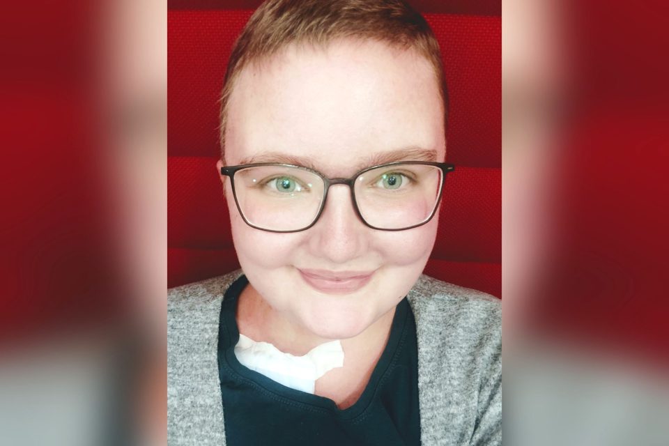 Lächelnde Frau mit Kurzhaarschnitt, am Kragen des T-Shirts ist ein Verband erkennbar.