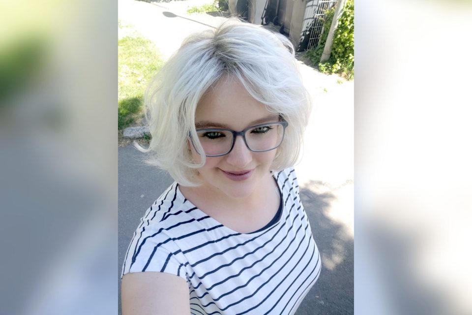 Fröhlich lächelnde Frau mit platinblonder Frisur in gestreiftem T-Shirt.