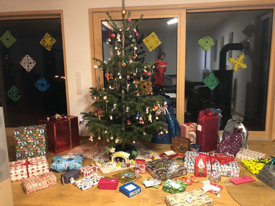 Bunt geschmückter Weihnachtsbaum mit vielen Geschenken am Boden in unterschiedlichsten Größen und Formen.