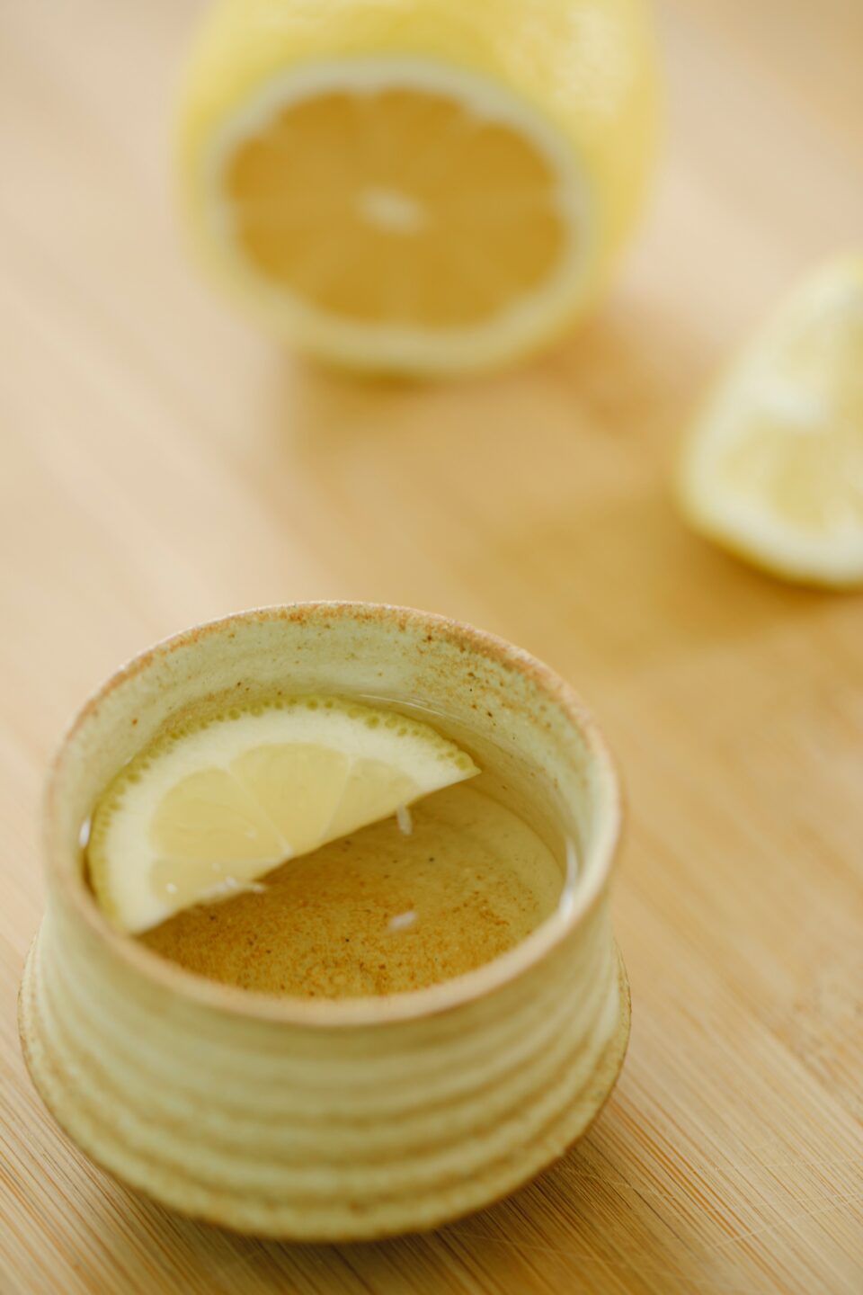 Tasse mit Getränk und einer halben Zitrone auf hellbrauner Tischplatte