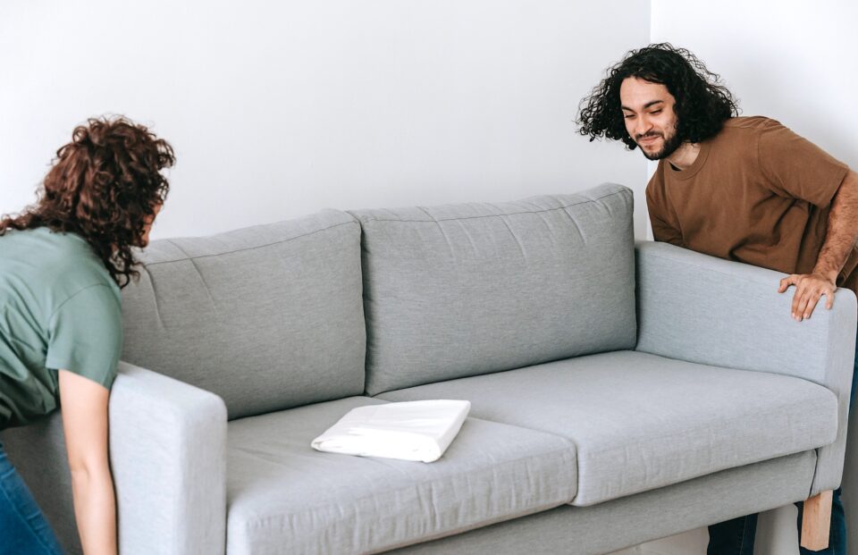 Eine Frau und ein Mann tragen gemeinsam ein Sofa.