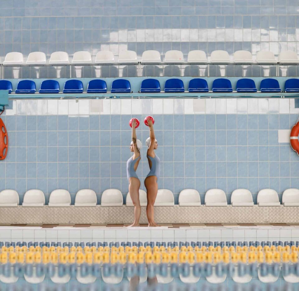 zwei Synchronschwimmerinnen machen eine Ballübung vor dem Pool