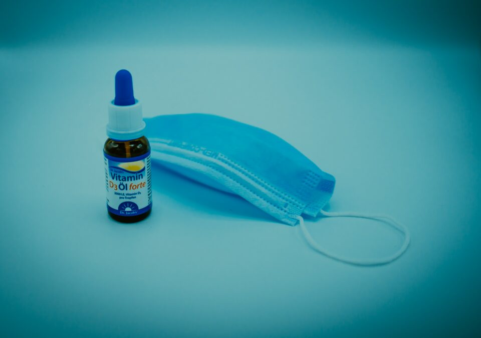 Blaue Covid-Maske neben Vitamin D3-Präparattropfen