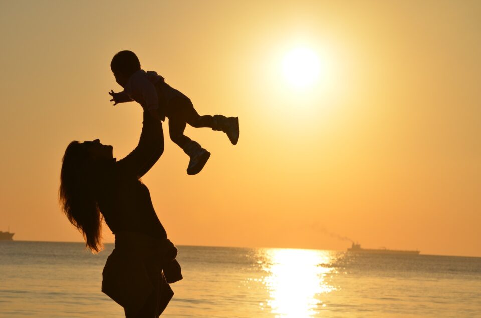 Sonnenbaby Mutter hält Kind in die Luft vor Sonnenuntergang am Meer