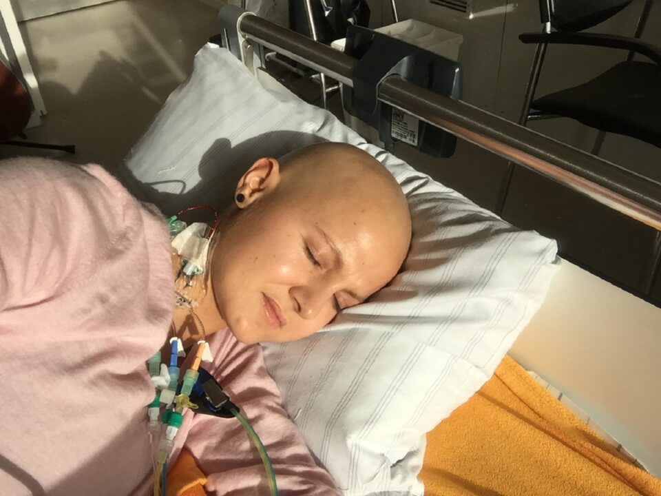 Raliza liegt mit einer Glatze und Port im Krankenhausbett