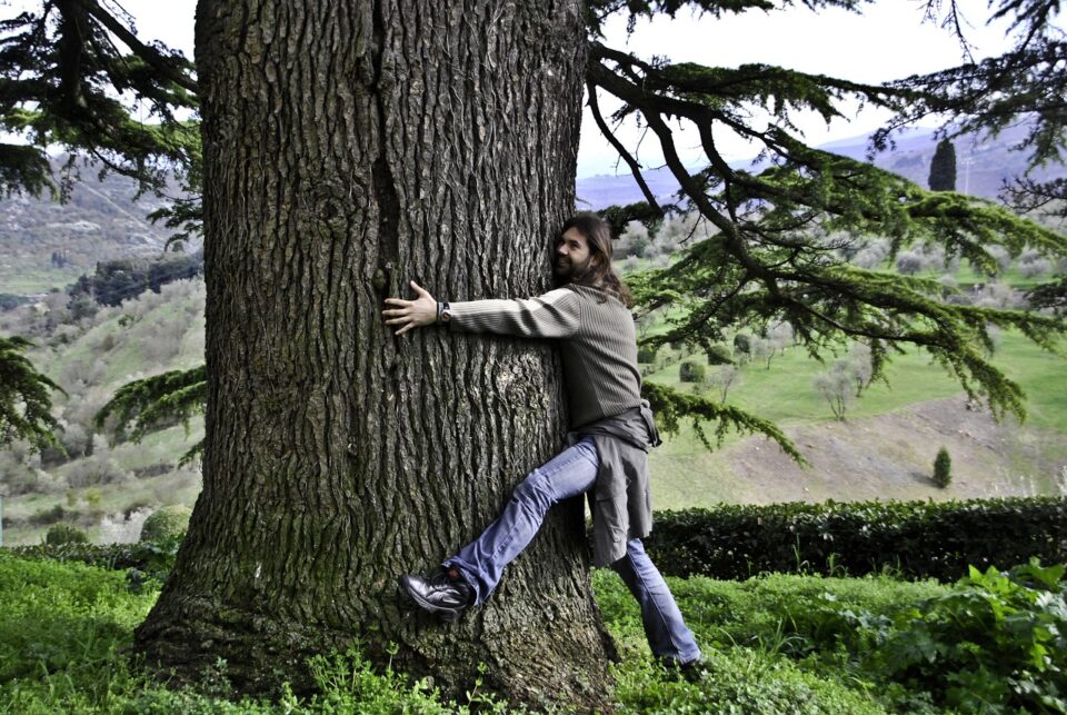 Ein langhaariger Mann, der einen Baum umarmt.