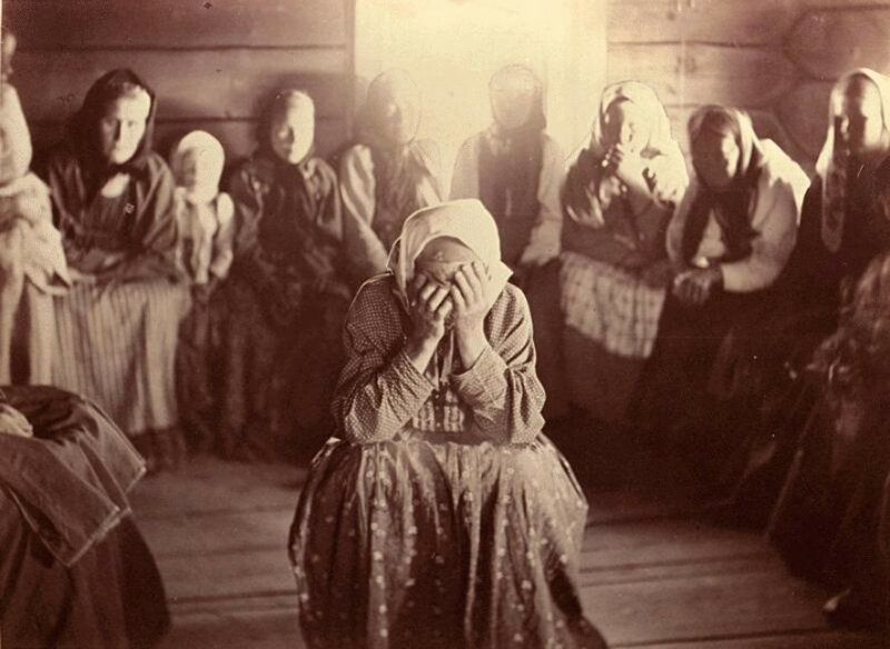 Eine russische Frau mit Kopftuch trauert inmitten einer Runde von Frauen.