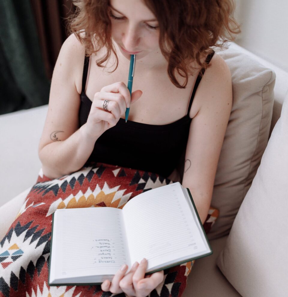 Frau mit Stift an den Lippen, die in ihr Notizbuch schaut