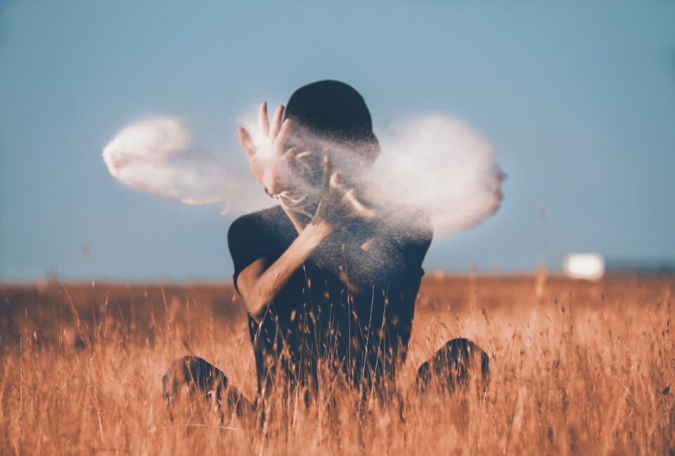 Person sitzt im Gras mit Nebel oder Rauch um den Kopf