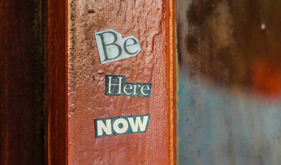 Worte Be here now auf Holzbalken