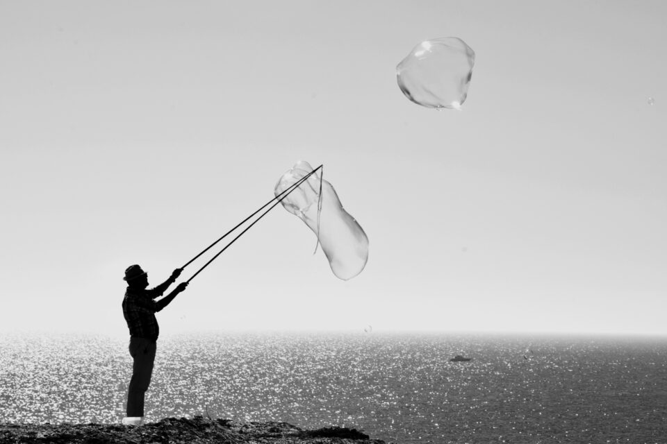 Mann steht am Meer und macht große Seifenblasen s/w