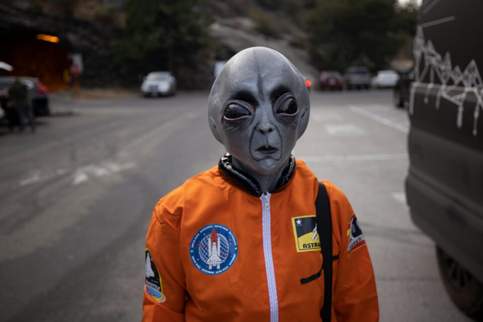 Als Alien verkleidete Person mit orangefarbenem Anzug und grauer Maske