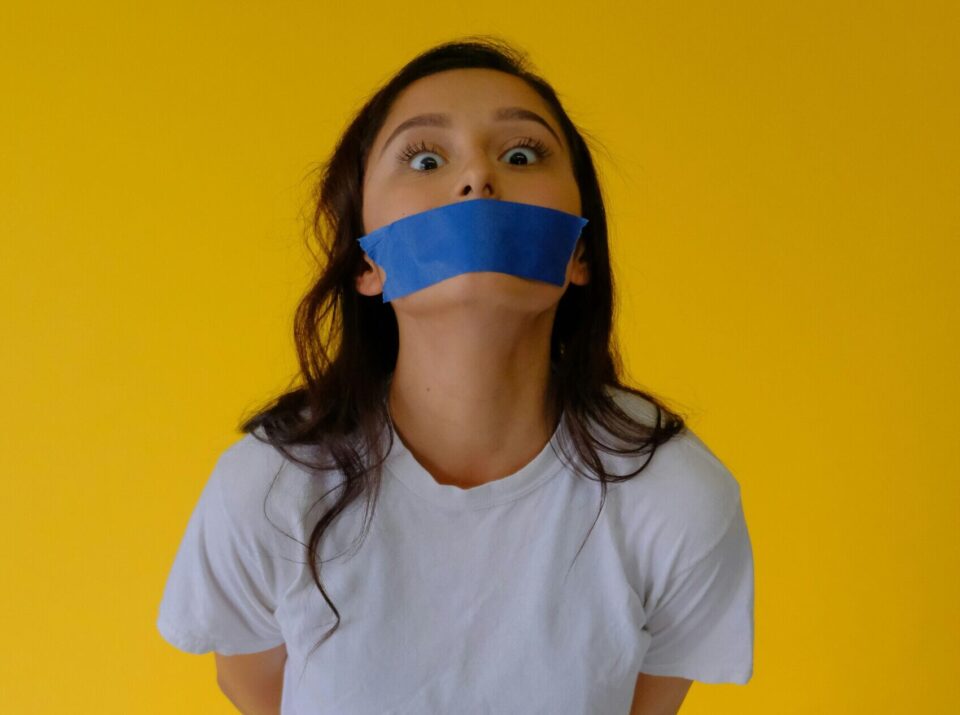 Frau vor gelbem Hintergrund mit blauem Tape über dem Mund