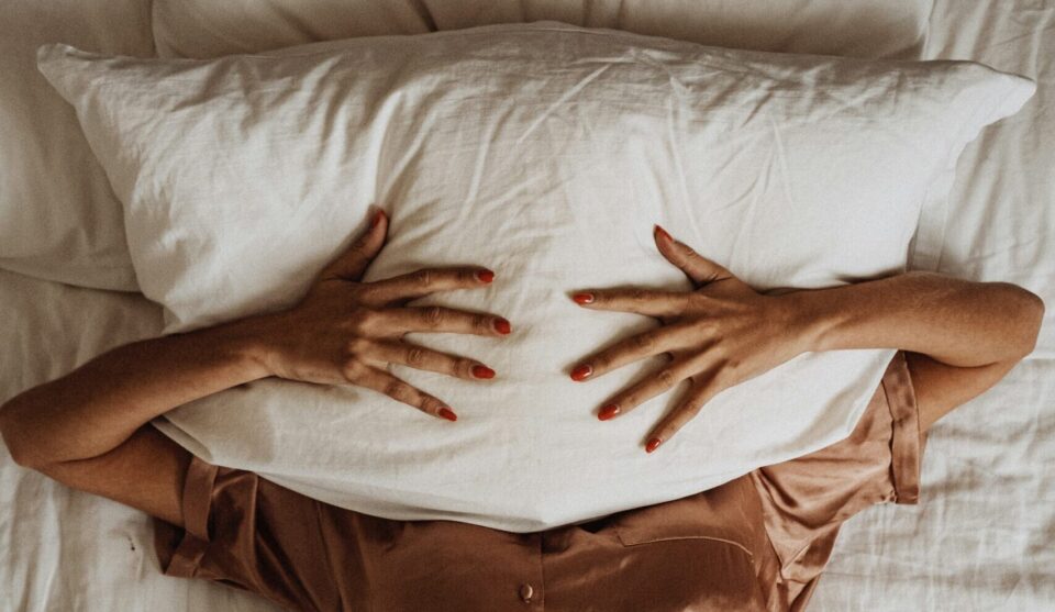 Frau hält sich Kopfkissen vors Gesicht