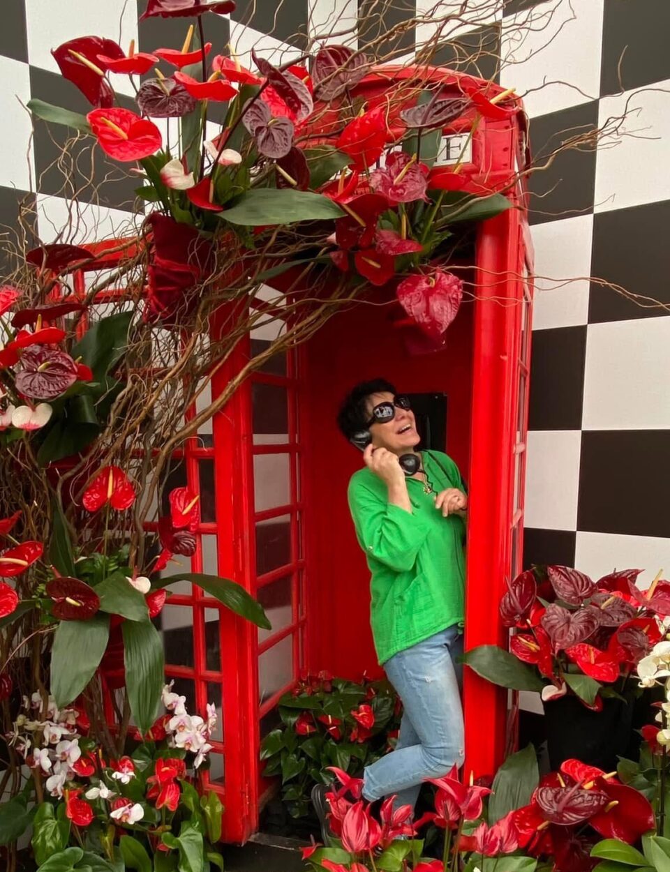 Frau steht in roter Telefonzelle mit Blumen ringsherum